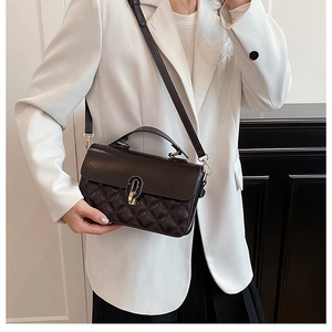 Close-up of a black quilted crossbody bag with metal buckle worn on a white blazer