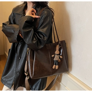 Detail of dark brown tote bag with geometric woven strap and plush rabbit charm accessory