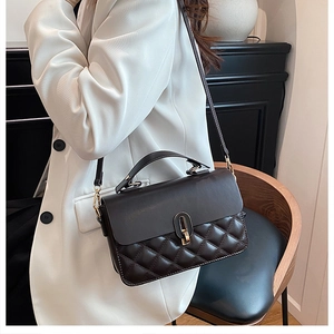 Detail of black quilted crossbody bag with gold hardware and stylish metal clasp on a model