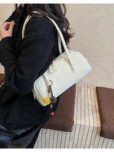 Detail view of cream leather Boston bag with decorative pompom charm and twin handles