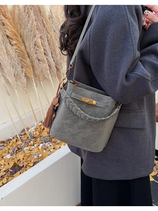 Close-up of gray frosted leather bucket bag with woven handle and tassel detail