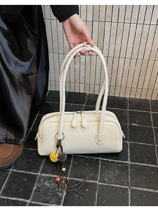 Detail of cream pebbled leather Boston bag with decorative pompom keychain and dual handles