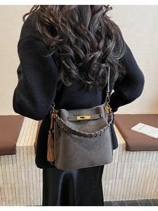 Detail of dark grey bucket bag with woven handle and gold clasp on a fashion model
