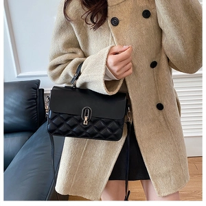 Detail of black quilted shoulder bag with golden twist lock on wool coat background