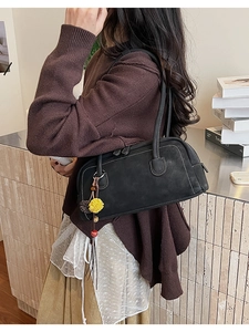 Detail of black underarm bag with contrast stitching and plush ball charm accessory