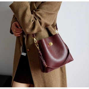 Detail of burgundy textured leather bucket bag with gold clasp on brown wool coat