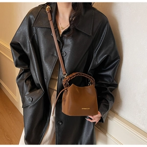 Detail view of brown bucket bag featuring woven handle and gold brand lettering