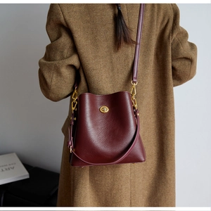 Detail view of burgundy leather bucket bag with gold clasp shown on a wool coat