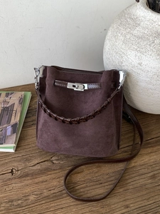 Dunkelbraune Wildleder-Beuteltasche mit geflochtenem Griff und Drehverschluss auf Holztisch