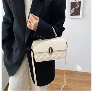 Close-up of beige quilted crossbody bag with black oval twist lock on a black blazer
