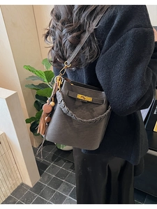 Detail of dark grey bucket bag featuring a gold twist lock and woven handle with tassels