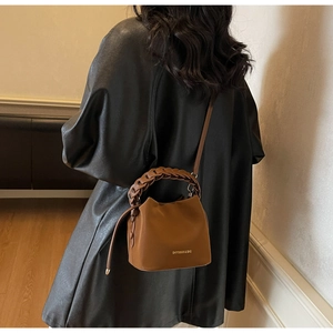 Close-up of brown suede bucket bag featuring a unique braided handle and gold embossed logo