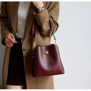 Detail of burgundy pebbled leather bucket bag featuring a golden turn-lock and crossbody strap