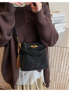 Detail of a black leather bucket bag with gold clasp and brown tassel fringe on a model