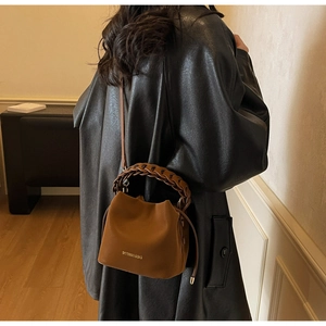 Brown lychee leather bucket bag with a braided handle and adjustable crossbody strap