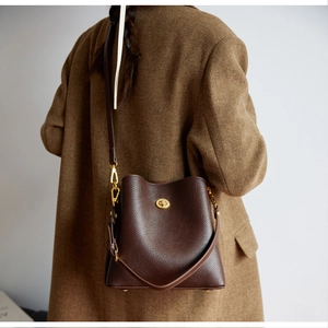 Detail of dark brown lychee leather bucket bag with gold turn-lock on wool coat