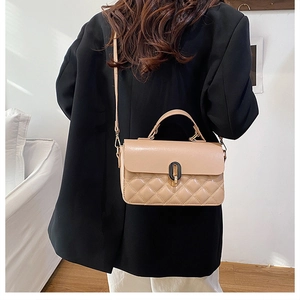 Quilted beige crossbody bag with oval turn-lock closure shown on shoulder of a model