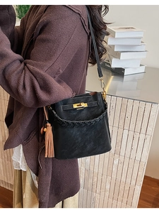 Detail of black pebbled leather bucket bag with woven handle and gold metal twist lock