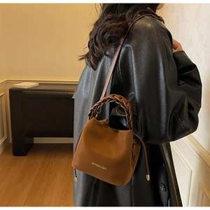 Close-up of caramel leather bucket bag with woven handle and drawstring detail