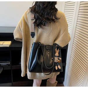 Detail of black faux leather tote bag with wide geometric strap and bunny charm