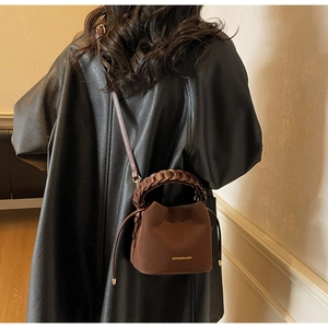 Detail of a dark brown bucket bag with braided handle worn over a black leather coat