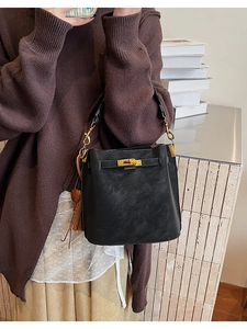Detail of black matte leather bucket bag featuring a golden turn-lock and leather tassel
