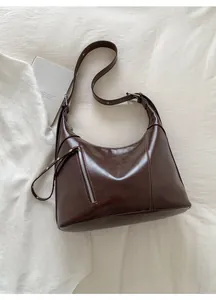 Detailed view of dark brown crescent bag with glossy leather and silver zipper accents