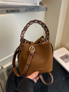 Brown PU leather bucket bag with woven handle and adjustable strap in a stylish setting