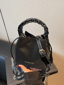 Minimalist black bucket bag with woven handle and gold logo on matte suede finish