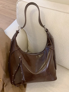 Vintage dark brown faux leather hobo bag with silver zippers on a white textured sofa