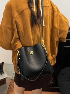 Woman wearing a large black pebbled leather bucket bag with a golden metallic twist lock