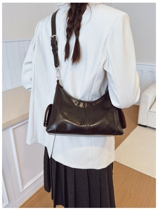Vue détaillée du sac bandoulière en cuir brillant noir porté avec un blazer blanc
