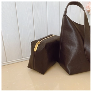 Detailed close-up of dark brown leather tote bag with gold zipper and pouch set