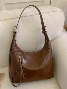Brown vintage leather hobo tote bag with front zipper pocket on a cream sofa
