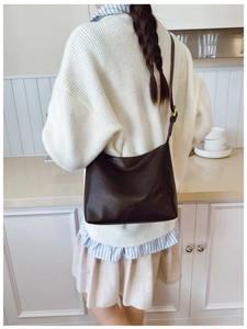 Detail of dark brown leather tote bag with subtle logo on minimalist soft surface