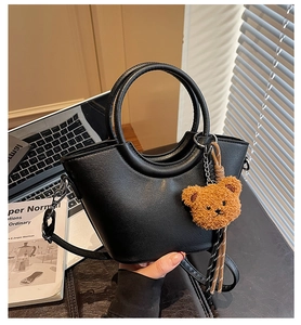 Detail of black faux leather handbag with round top handle and cute brown plush bear charm