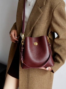 Minimalist burgundy leather bucket bag with pebble texture and gold twist lock closure