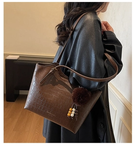 Close-up of brown crocodile texture tote bag with plush charm on black winter coat