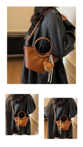 Detail of brown bucket bag with round handle, plush bear charm and striped scarf detail
