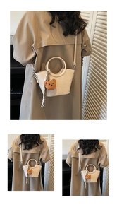 Detail of cream mini bucket bag with round handle and plush bear charm on camel coat