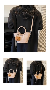 Detail view of beige crescent handbag featuring a cute plush bear charm and striped ribbon