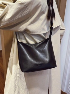 Minimalist black leather oversized tote bag shown on model with beige trench coat
