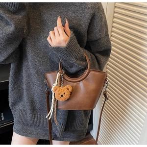 Detail of dark brown leather handbag with teddy bear charm and checkered scarf accent