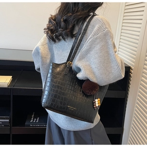 Detail of black stone-patterned leather tote bag with pompom charm and logo text