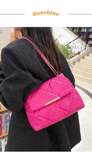 Close-up of rose red quilted chain bag on black coat with minimalist metal lock