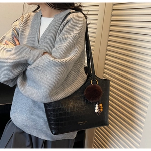 Close-up of black croc-effect tote bag with branding and brown pom-pom charm detail