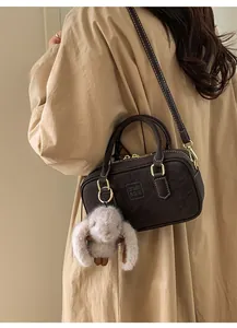 Detail of dark coffee Boston bag with gold hardware and plush rabbit charm on model