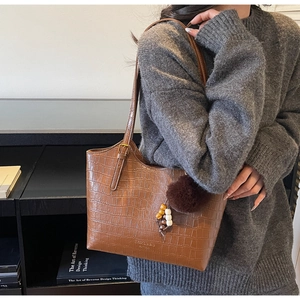 Detail of vintage brown crocodile embossed tote bag with fuzzy ball charm and shoulder strap