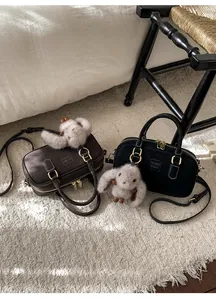 Close-up of Boston style handbags in black and brown with plush rabbit pendants