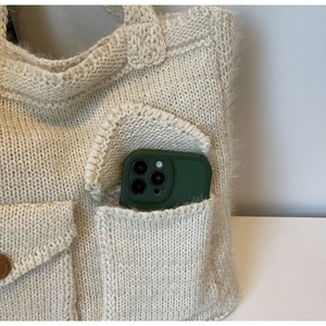 Macro detail of cream knit tote bag showing a side pocket with a green phone inside